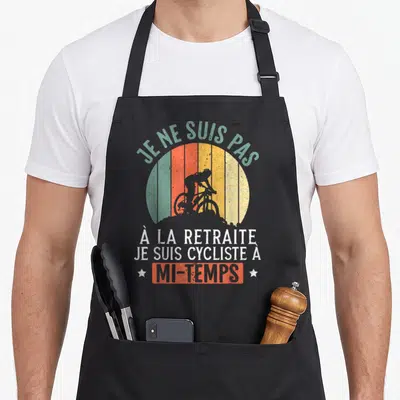 Tablier de cuisine noir avec silhouette de cycliste et texte humoristique sur fond de soleil multicolore.
