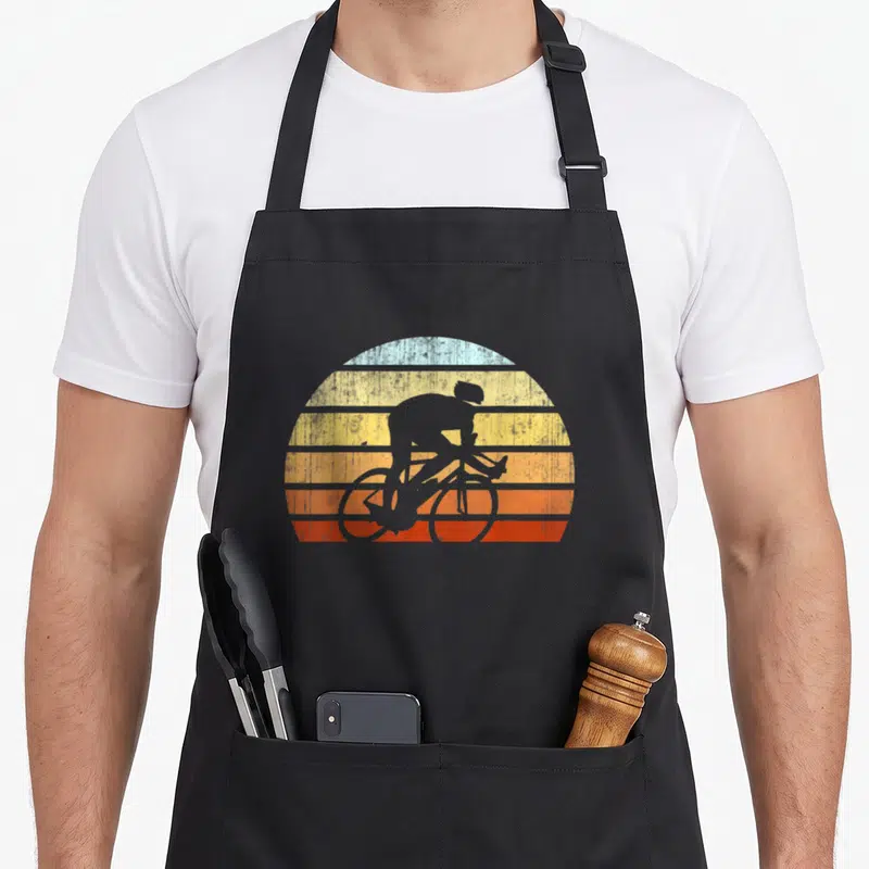 Tablier de cuisine noir avec silhouette cycliste sur fond de soleil vintage aux bandes colorées dégradées.