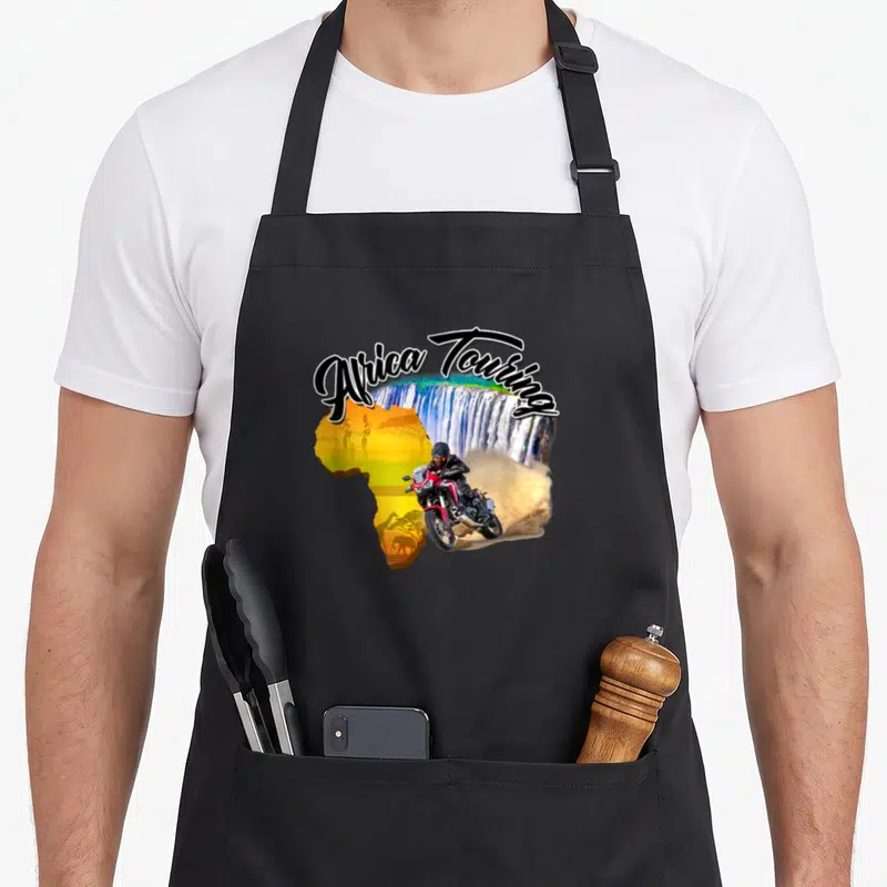 Tablier de cuisine noir avec illustration d'une moto rouge traversant une carte d'Afrique colorée devant un grand waterfall.