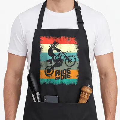 Tablier de cuisine noir avec silhouette de motard freestyle sur fond de bandes colorées vintage et texte Ride or Die.
