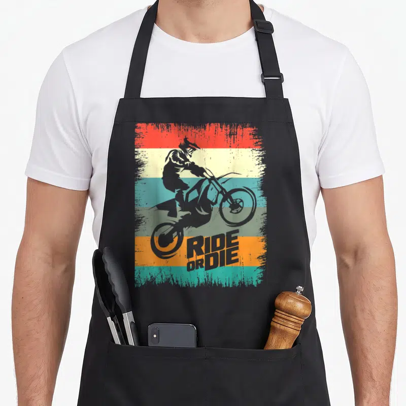 Tablier de cuisine noir avec silhouette de motard freestyle sur fond de bandes colorées vintage et texte Ride or Die.