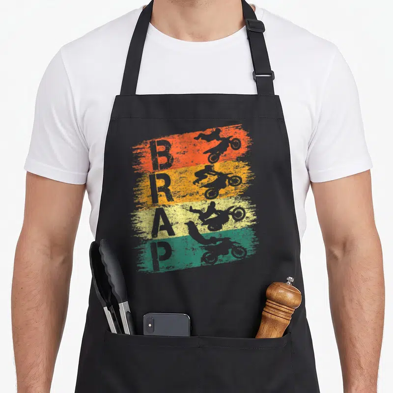 Tablier de cuisine noir avec motif Brap vintage, silhouettes de dirt bikes et bandes orange jaune vert turquoise.