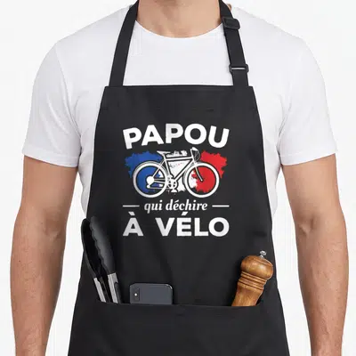 Tablier de cuisine noir avec motif Papou qui déchire à vélo et tricycle blanc sur fond tricolore.