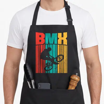 Tablier de cuisine noir avec une illustration vintage représentant un cycliste BMX devant des lettres colorées et des bandes verticales.