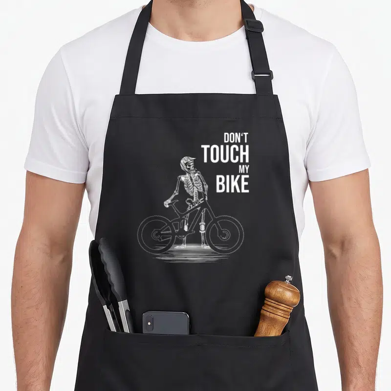 Tablier de cuisine noir avec illustration blanche d'un squelette en casque de VTT tenant son vélo.