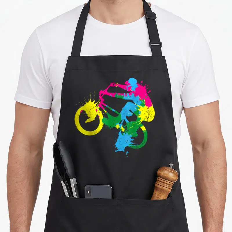 Tablier de cuisine noir avec silhouette cycliste BMX aux couleurs vives et effet éclaboussure artistique.