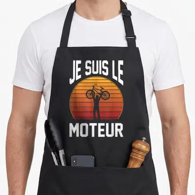 Tablier de cuisine noir avec silhouette cycliste et texte Je suis le moteur sur fond de soleil retro orange et rouge.