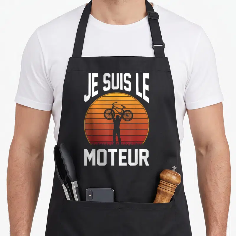 Tablier de cuisine noir avec silhouette cycliste et texte Je suis le moteur sur fond de soleil retro orange et rouge.