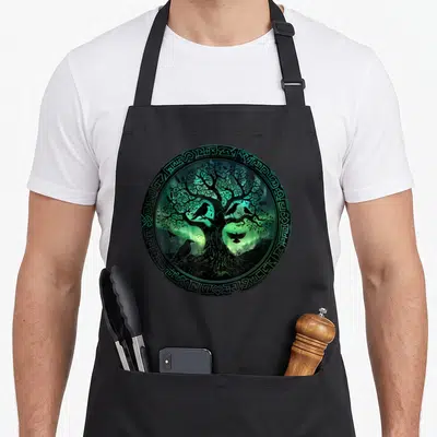 Tablier de cuisine noir avec illustration circulaire d'un arbre aux branches complexes et de corbeaux sur fond vert luminescent.