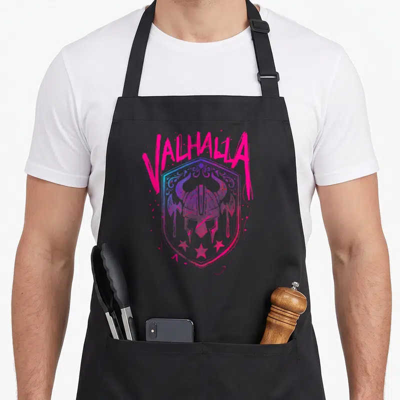 Tablier de cuisine noir avec bouclier rose et bleu, casque viking et texte Valhalla en style graffiti.