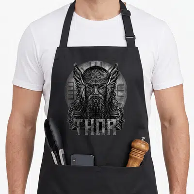 Tablier de cuisine noir avec illustration gravée de Thor dieu viking aux ailes et runes en arrière-plan.