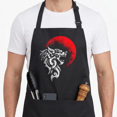 Tablier de cuisine noir avec tête de loup Fenrir stylisée en blanc devant un cercle rouge texturé.
