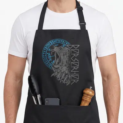 Tablier de cuisine noir avec tête d'ours berserker, runes circulaires bleues et inscription verticale stylisée en gris foncé.