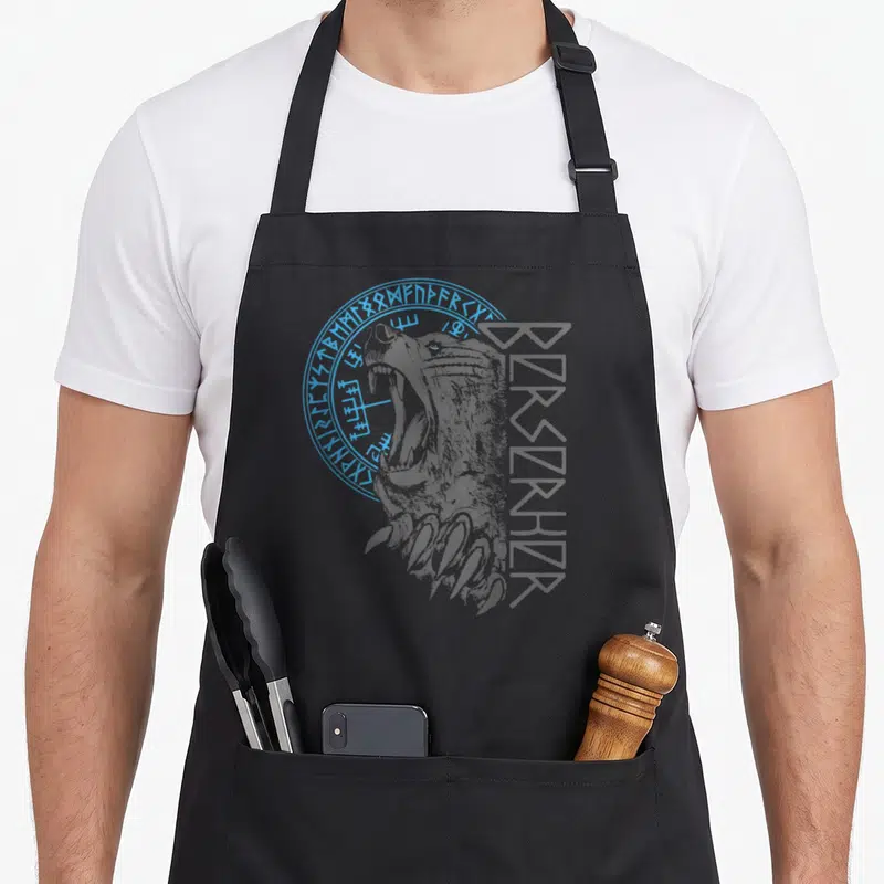 Tablier de cuisine noir avec tête d'ours berserker, runes circulaires bleues et inscription verticale stylisée en gris foncé.