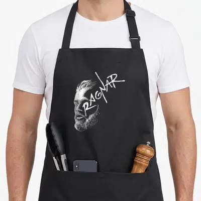 Tablier de cuisine noir avec portrait stylisé en blanc d'un homme à la barbe et le mot Ragnar écrit en lettres anguleuses sur le front.