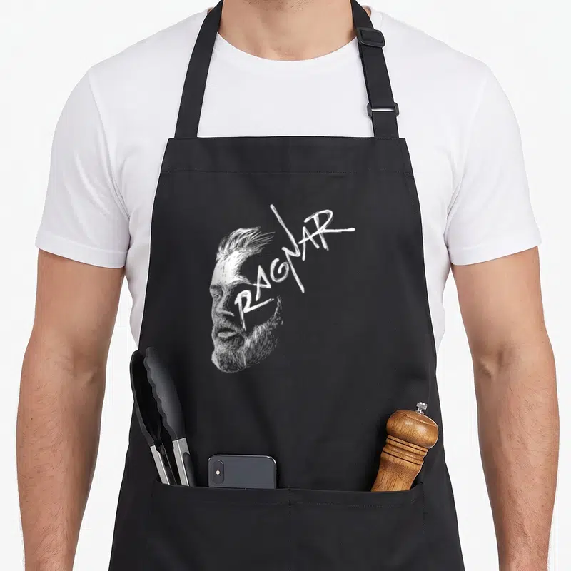 Tablier de cuisine noir avec portrait stylisé en blanc d'un homme à la barbe et le mot Ragnar écrit en lettres anguleuses sur le front.