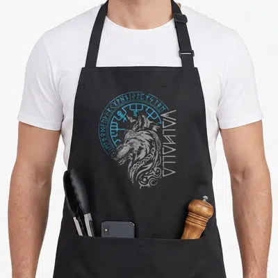Tablier de cuisine noir avec tête de loup gris, cercle runique bleu et texte vertical Walhalla sur le côté droit.