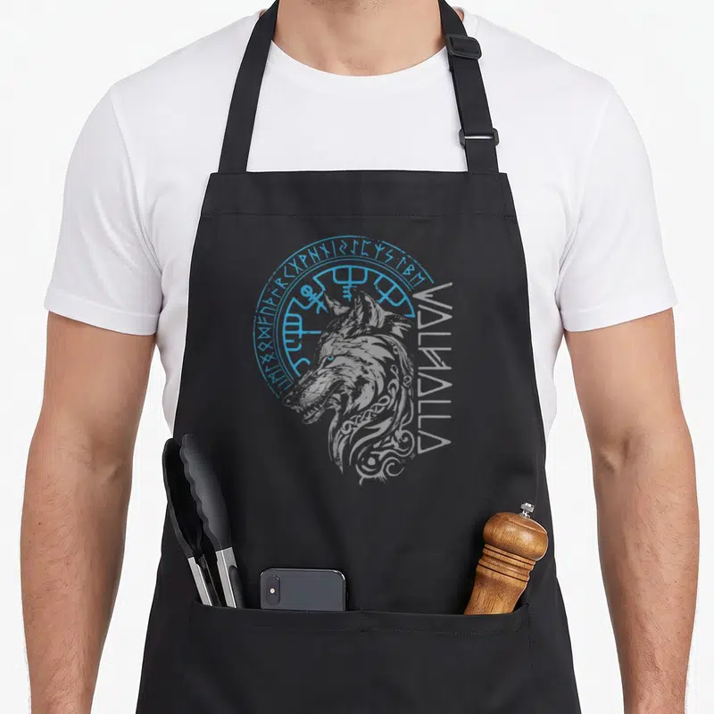 Tablier de cuisine noir avec tête de loup gris, cercle runique bleu et texte vertical Walhalla sur le côté droit.