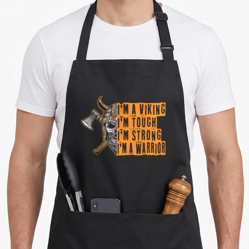 Tablier de cuisine noir avec illustration d'un crâne viking à la hache et texte en anglais sur bandes oranges.