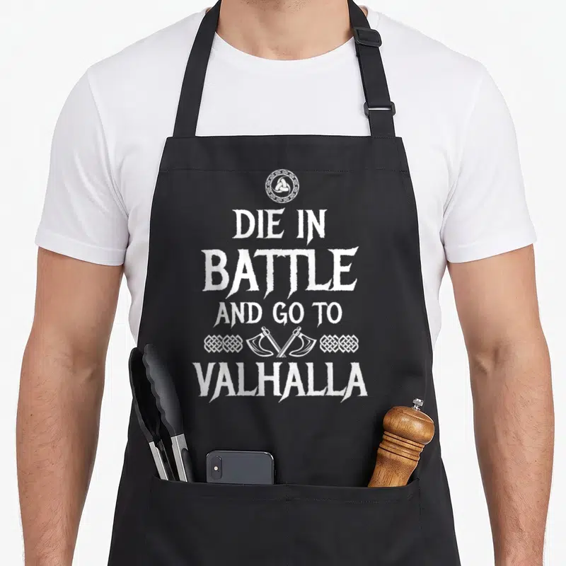 Tablier de cuisine noir avec inscription Die in battle and go to Valhalla et deux haches croisées en blanc.