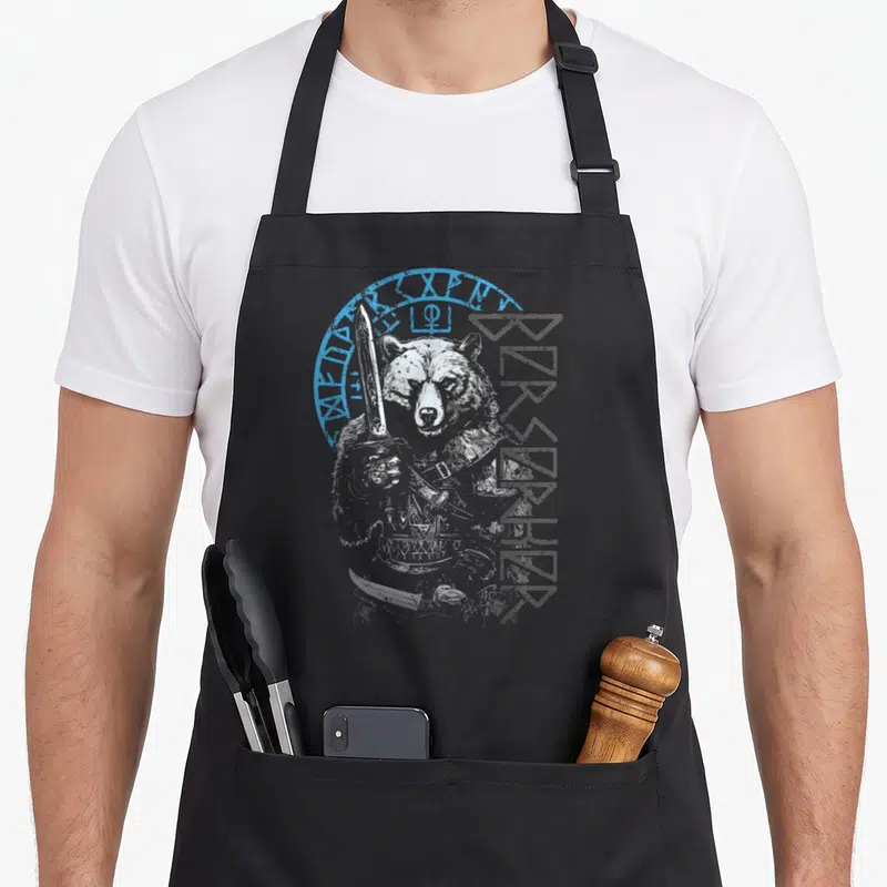 Tablier de cuisine noir avec illustration d'un ours berserker tenant une lame et des runes nordiques.