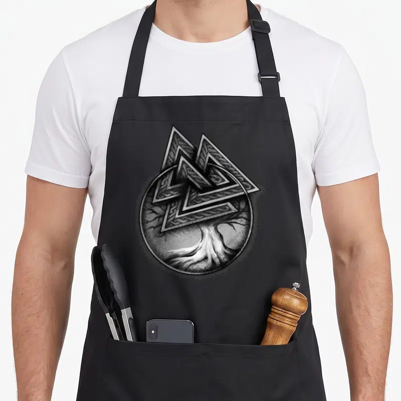 Tablier de cuisine noir avec un arbre de vie aux racines fines et un symbole valknut géométrique en haut du motif circulaire.