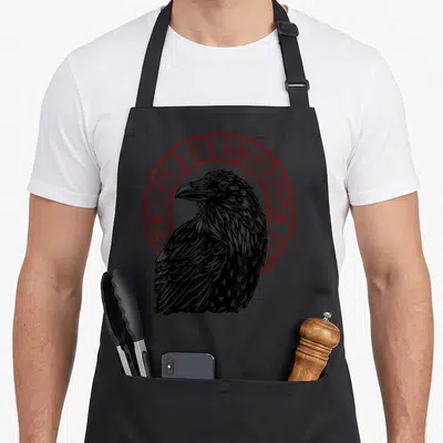 Tablier de cuisine noir avec illustration corbeau et cercle de runes rouges stylisées.
