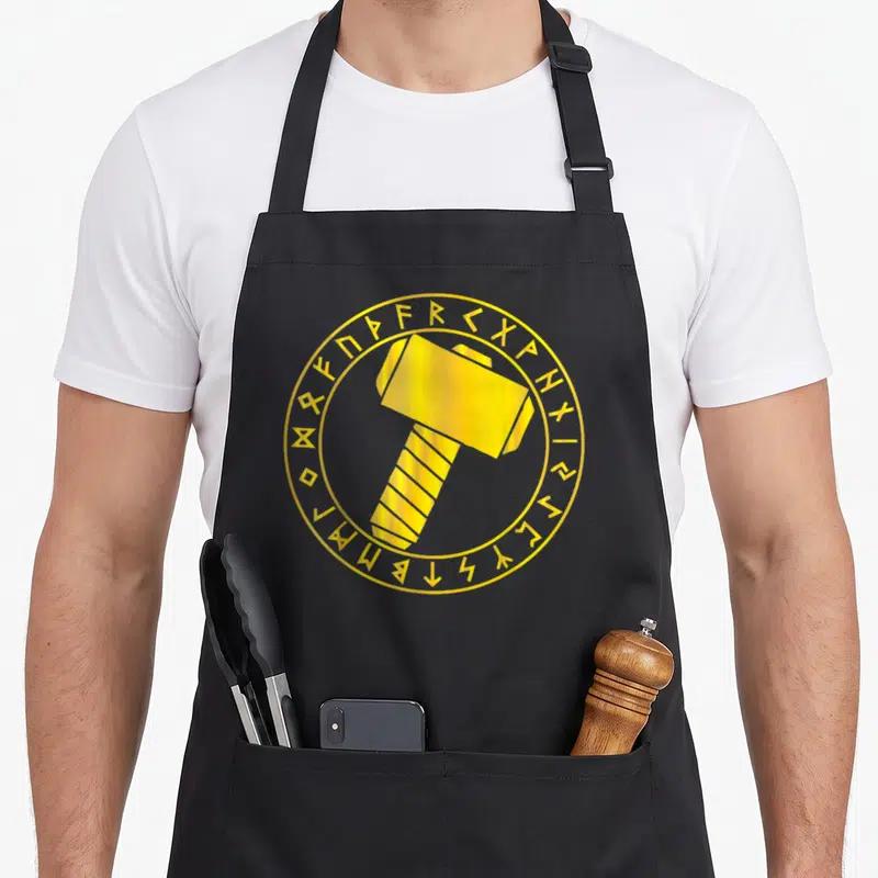 Tablier de cuisine noir avec illustration dorée du marteau Mjolnir entouré de runes nordiques en cercle.