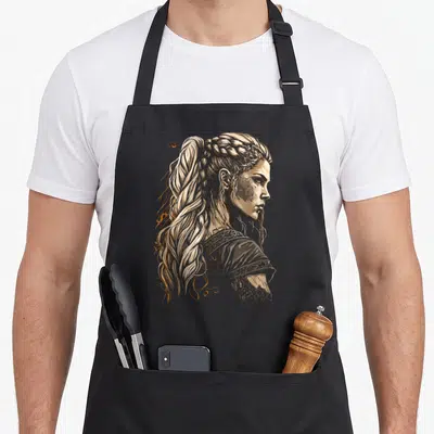 Tablier de cuisine noir avec illustration de profil d'une femme viking aux longs cheveux tressés et détails artistiques orange.