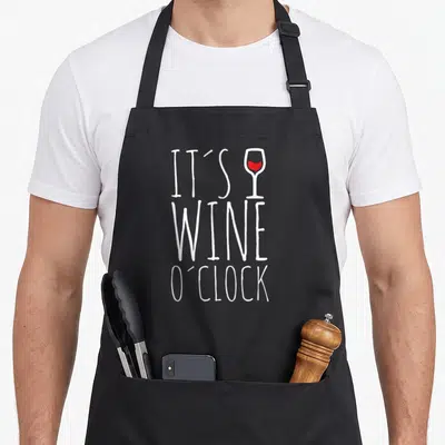 Tablier de cuisine noir avec inscription It's Wine O'Clock et verre à vin rouge stylisé en blanc et rouge.