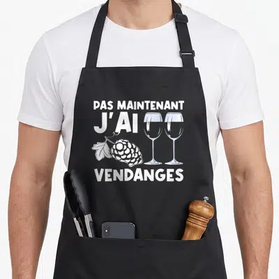 Tablier de cuisine noir avec texte blanc Pas Maintenant J'ai Vendanges, deux verres à vin et grappe de raisin stylisée.