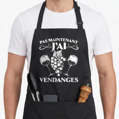Tablier de cuisine noir avec illustration blanche d'une grappe de raisin entre deux verres de vin et texte humoristique.