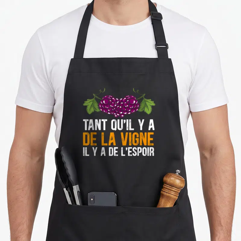 Tablier de cuisine noir avec un cœur formé de grappes de raisin violet et le texte Tant qu'il y a de la vigne il y a de l'espoir.