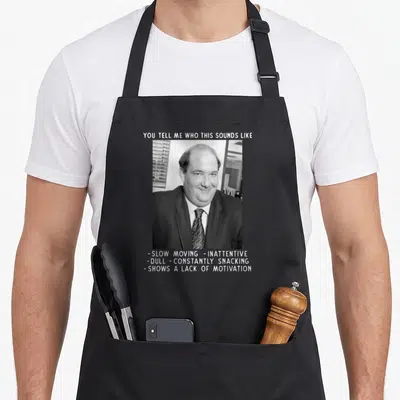Tablier de cuisine noir avec portrait en noir et blanc d'un homme en costume et texte humoristique en anglais au-dessus et en dessous.