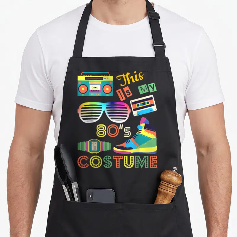 Tablier de cuisine noir avec une boombox, des lunettes à rayures, une cassette et le texte This is My 80s Costume en couleurs vives.