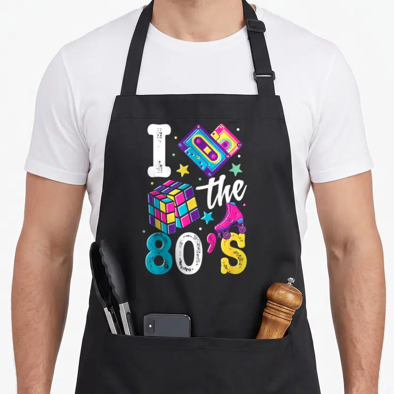 Tablier de cuisine noir avec illustration I the 80's, cassettes audio, cube de Rubik et patins roses aux couleurs vives.