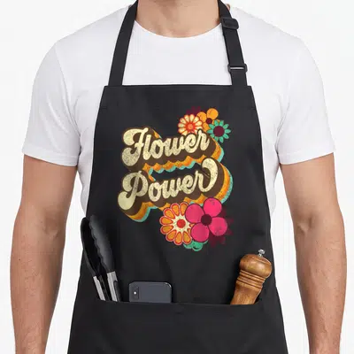 Tablier de cuisine noir avec inscription Flower Power et fleurs colorées dans un style rétro des années soixante.