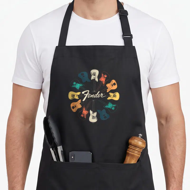 Tablier de cuisine noir avec un motif circulaire de guitares électriques colorées et le logo Fender en blanc.
