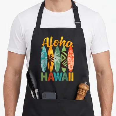 Tablier de cuisine noir avec cinq planches de surf hawaïennes colorées et le texte Aloha Hawaii en lettres rétro.