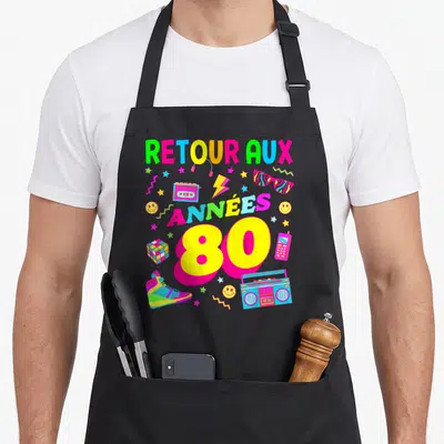 Tablier de cuisine noir avec inscription « Retour aux Années 80 » entourée de boombox, ruban magnétique et sneakers colorées.