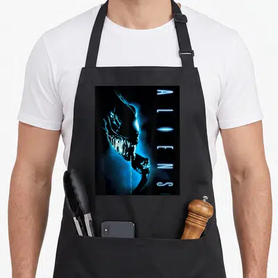 Tablier de cuisine noir avec illustration bleue du Xenomorph et texte ALIENS vertical sur fond sombre.