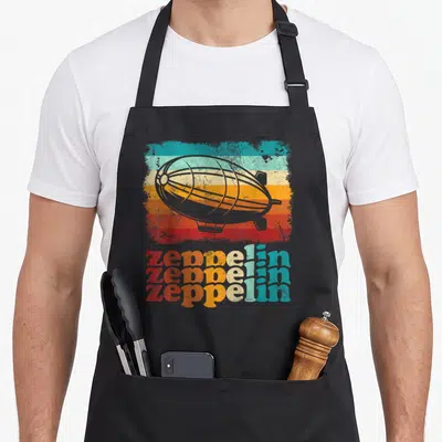 Tablier de cuisine noir avec illustration d'un dirigeable gris sur bandes colorées sunset et texte Zeppelin en trois lignes délavées rouge orange et turquoise.