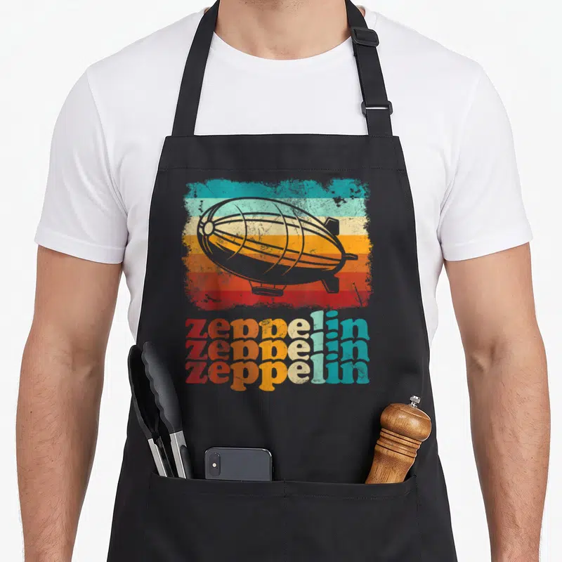 Tablier de cuisine noir avec illustration d'un dirigeable gris sur bandes colorées sunset et texte Zeppelin en trois lignes délavées rouge orange et turquoise.