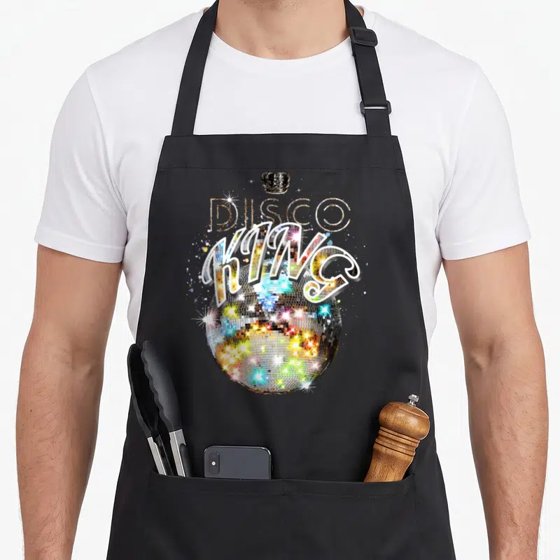 Tablier de cuisine noir avec une boule disco multicolore, une couronne noire et l'inscription Disco King en lettres stylisées.