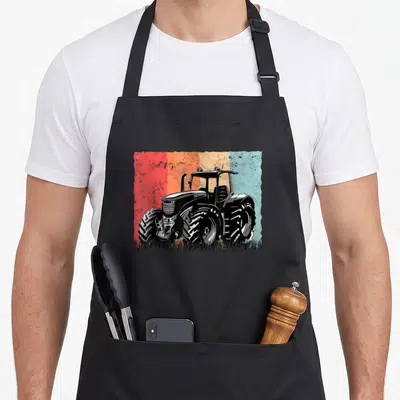 Tablier de cuisine noir avec illustration d'un tracteur retro Bauers Trekker sur fond multicolore texturé rouge orange beige et bleu.