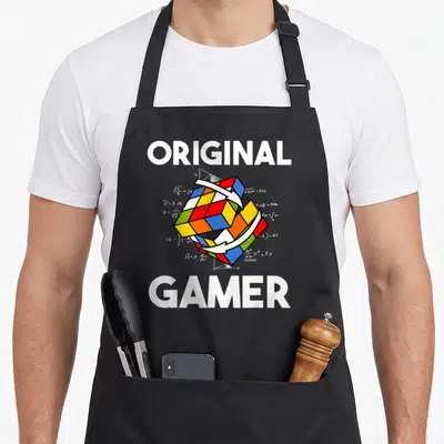 Tablier de cuisine noir avec illustration de cube de Rubik, formules mathématiques et texte Original Gamer en blanc.