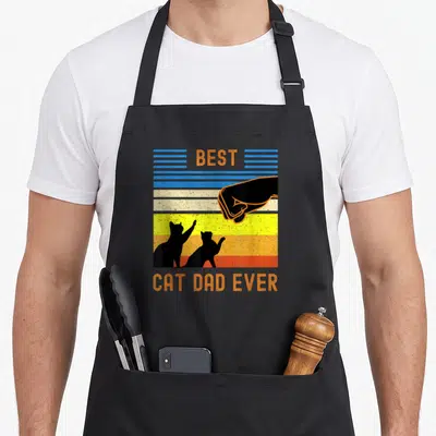 Tablier de cuisine noir avec design vintage Best Cat Dad Ever et poignée de main entre humain et chats en silhouette.