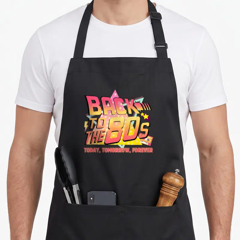 Tablier de cuisine noir avec graphisme Back to the 80s, cassette et étoiles colorées.