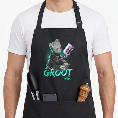 Tablier de cuisine noir avec Groot tenant une cassette rose et turquoise sur fond à pois halos.