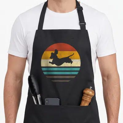 Tablier de cuisine noir avec silhouette de teckel gris sur fond de soleil rayé orange jaune turquoise et beige style rétro.